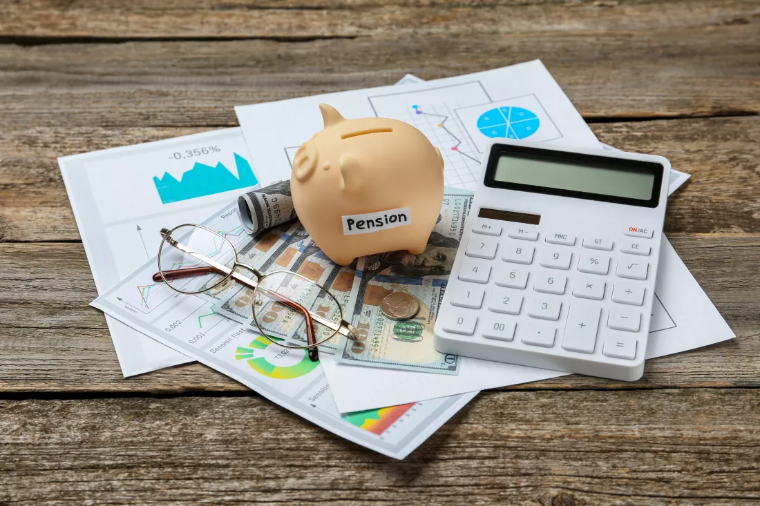piggy-bank-with-word-pension-banknotes-glasses-calculator-diagrams-wooden-table-retirement-savings