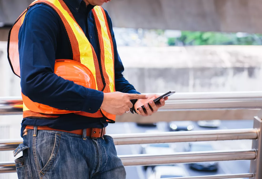 midsection-man-holding-hardhat-while-using-mobile-phone-railing