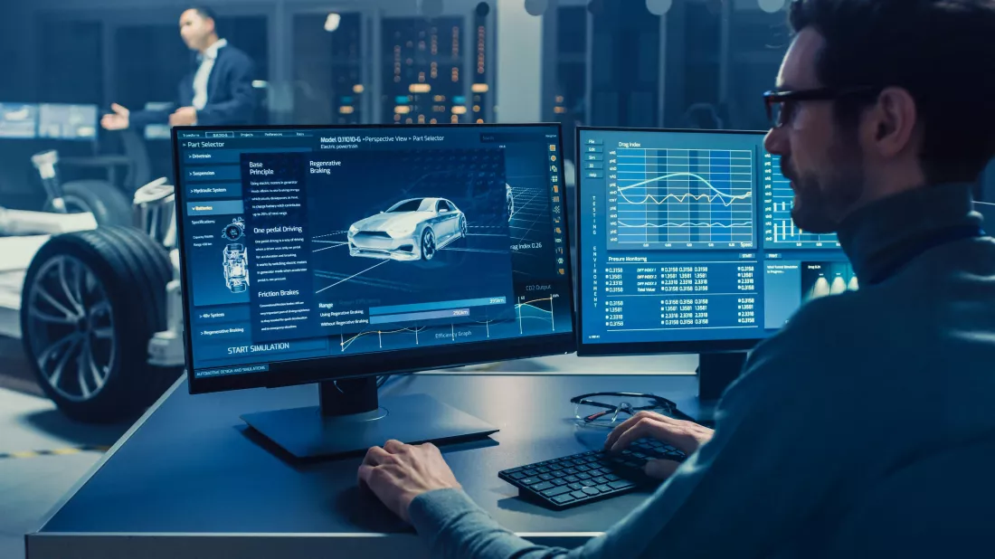 man-sits-desk-front-two-computer-monitors-with-car-screen